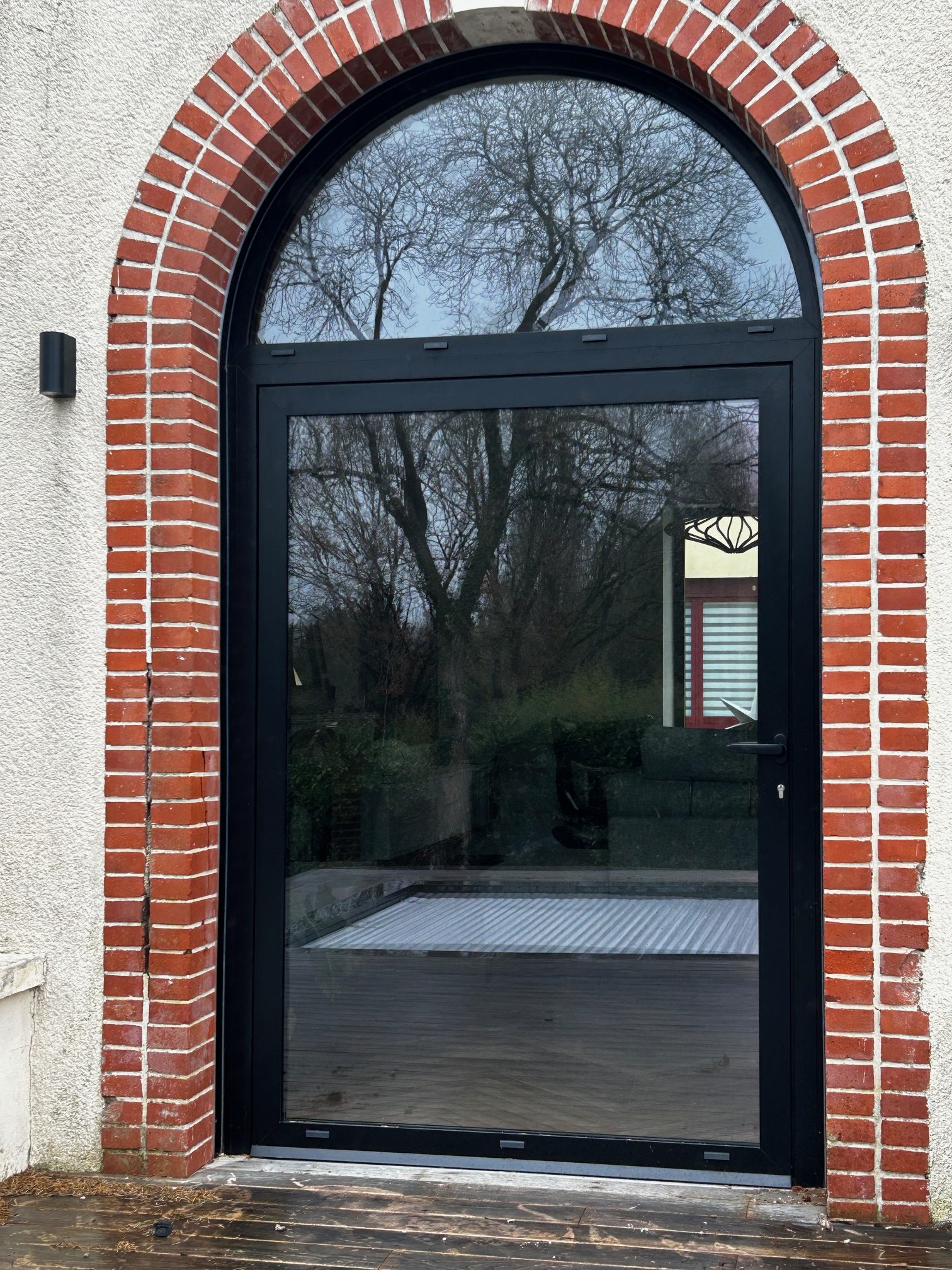 Porte-fenêtre cintrée en aluminium noir posée sur une façade en briques par Bonno Ouvertures, près de Nantes.