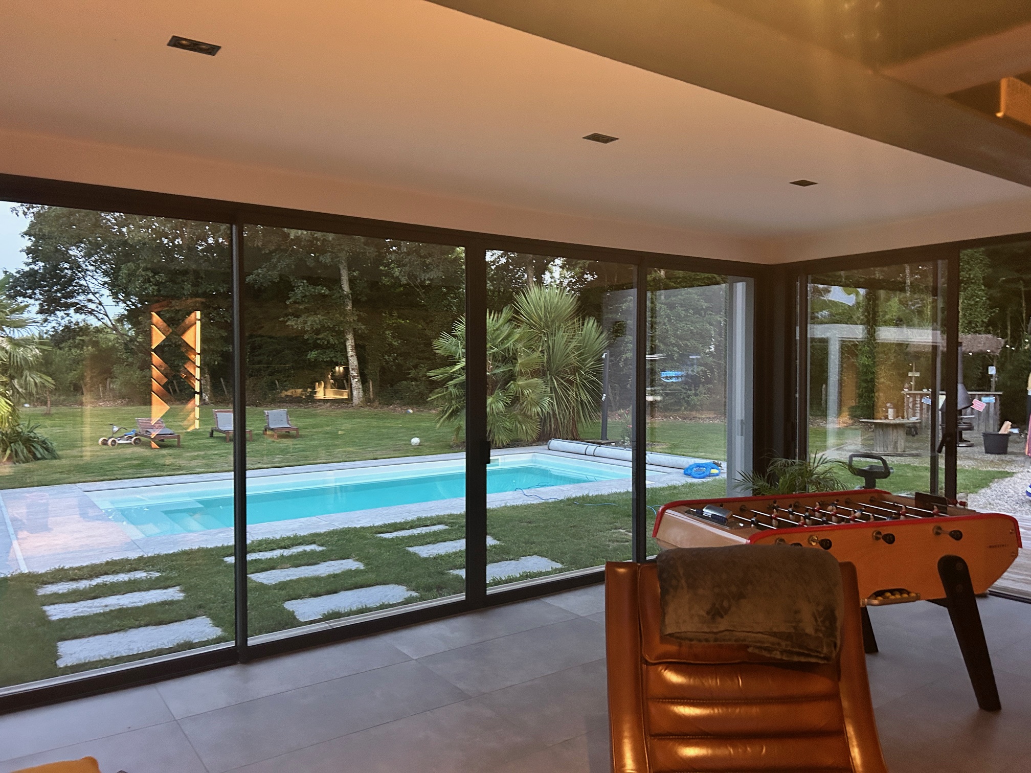 Baies vitrées aluminium sur mesure installées par Bonno Ouvertures, avec vue sur piscine depuis une pièce de vie moderne.