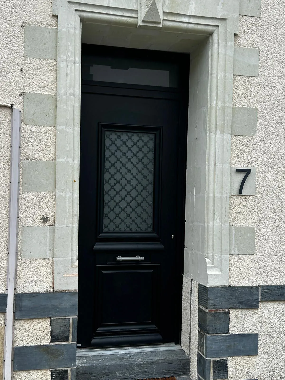 Porte d’entrée traditionnelle noire avec vitrage décoratif, posée sur une façade ancienne en pierre par Bonno Ouvertures.