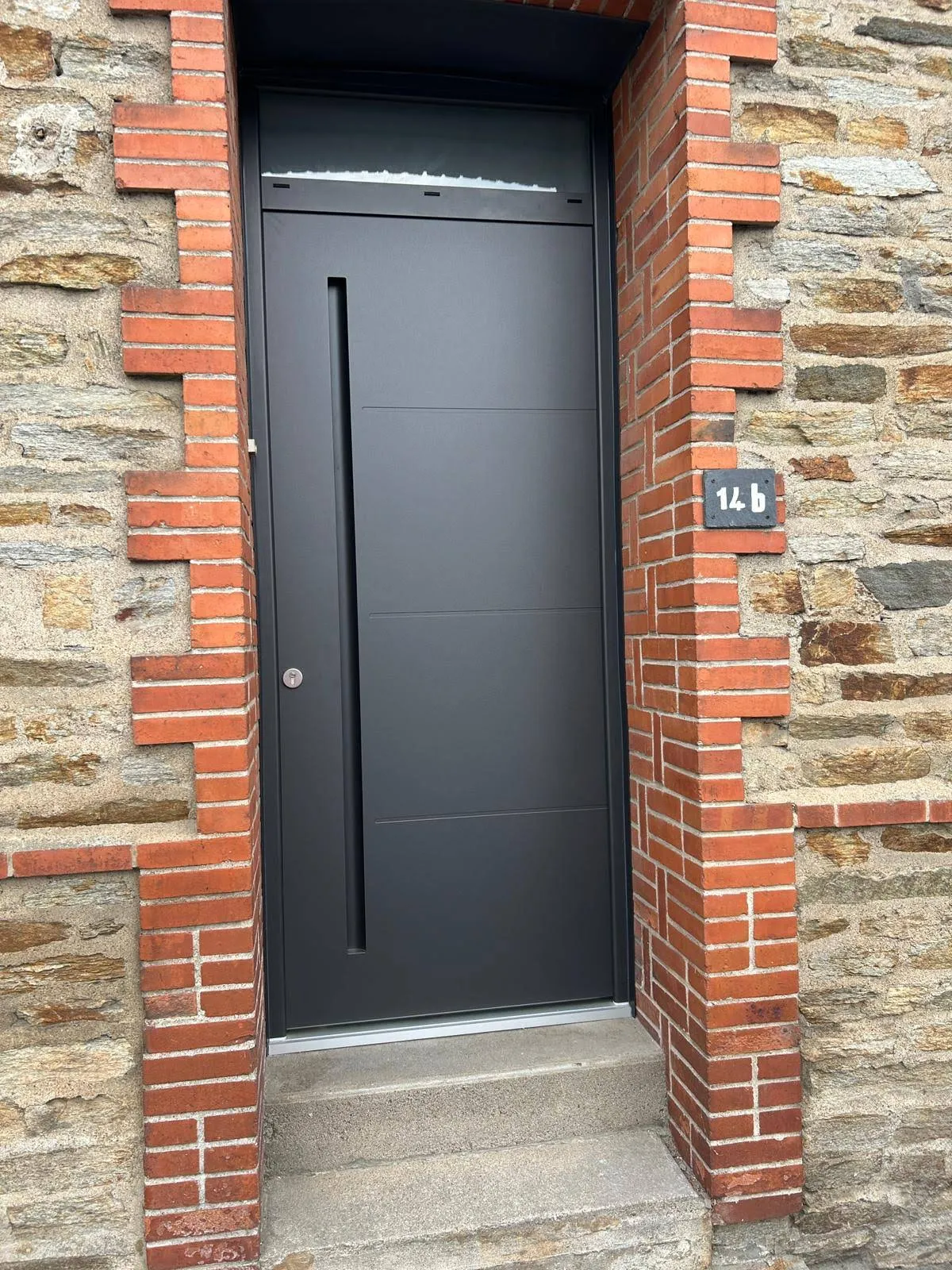 Porte d’entrée contemporaine en aluminium gris anthracite posée sur une maison en pierre, par Bonno Ouvertures.
