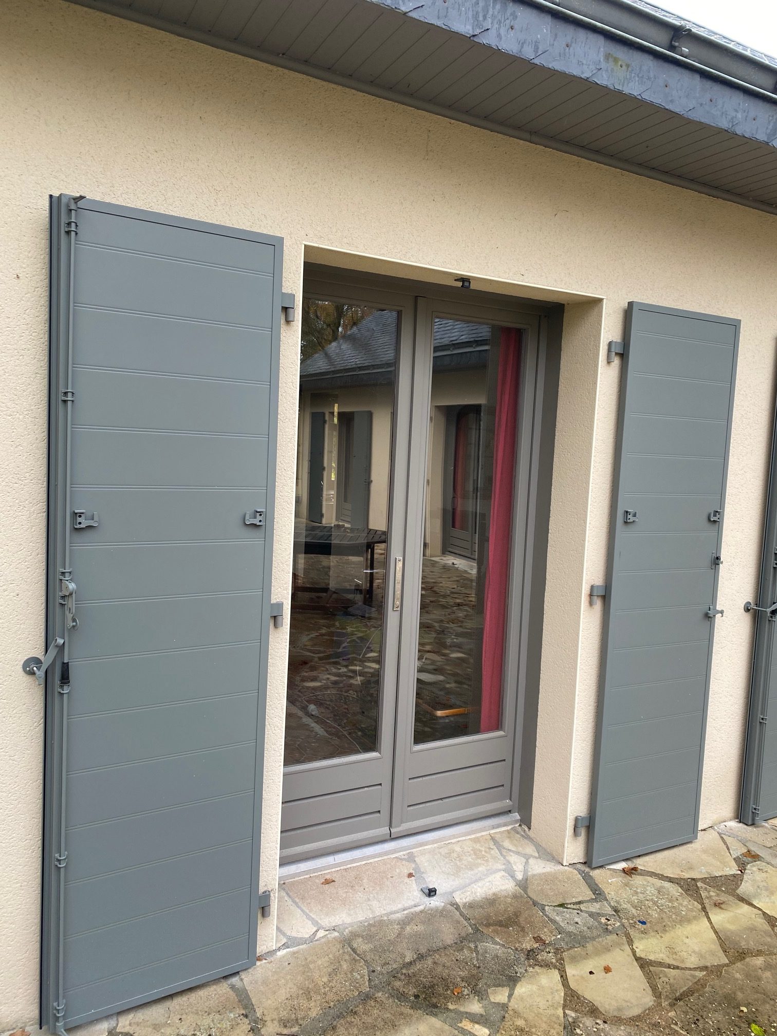 Volets battants en aluminium gris clair posés sur une porte-fenêtre, par Bonno Ouvertures en Loire-Atlantique.