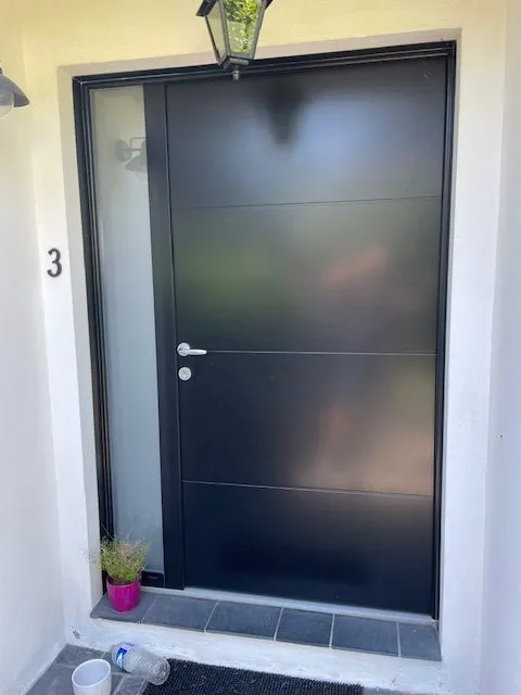 Porte d’entrée pleine en aluminium avec vitrage latéral, posée sur une maison individuelle par Bonno Ouvertures.